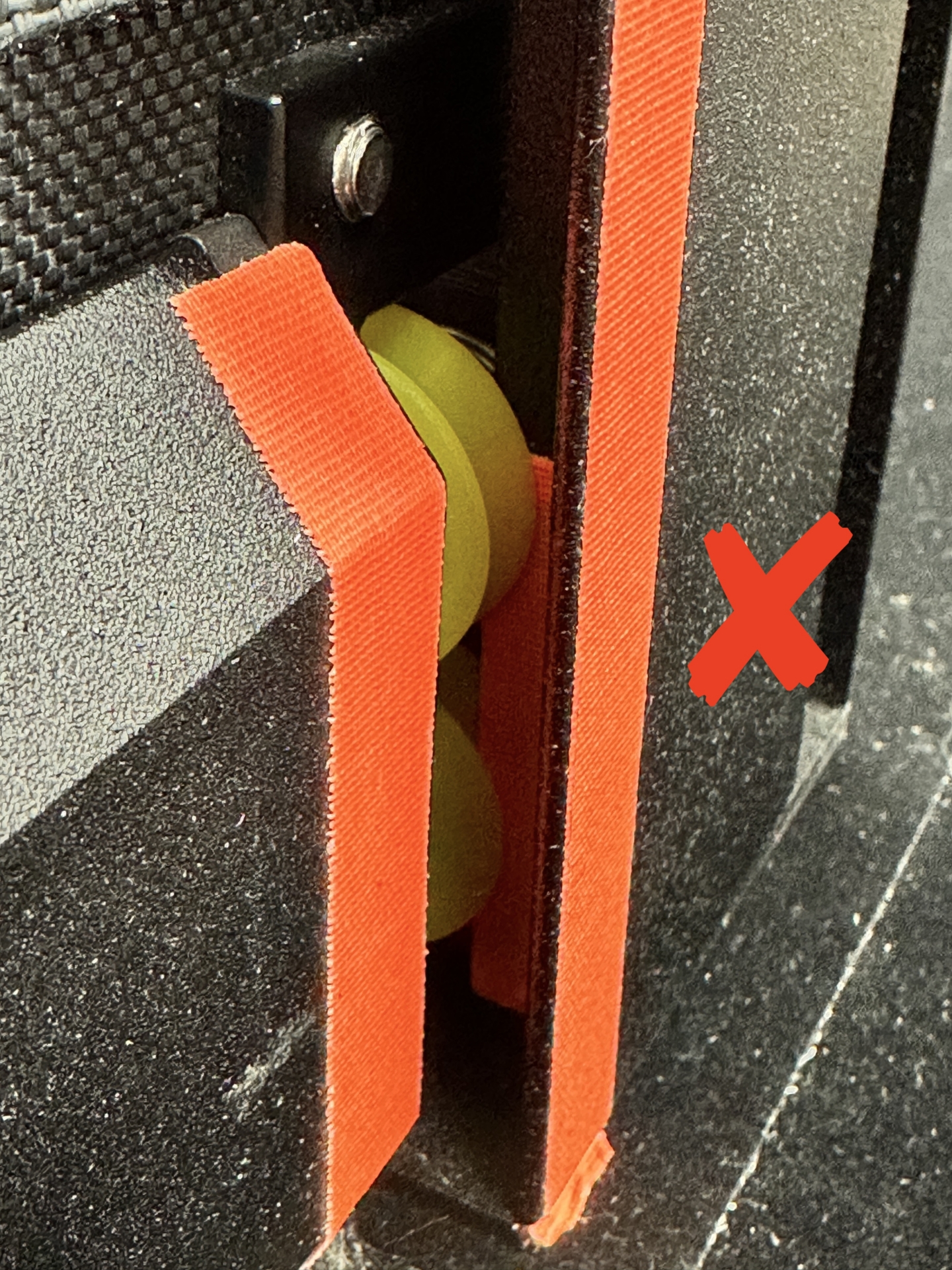 Orange strap incorrectly routed around yellow roller wheel, marked with red X