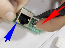 Fingers inserting flat ribbon cable into green circuit board with ethernet port, arrows indicating cable direction