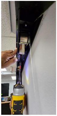 Hand holding drill securing spring cassette to mounting surface above roller shade housing