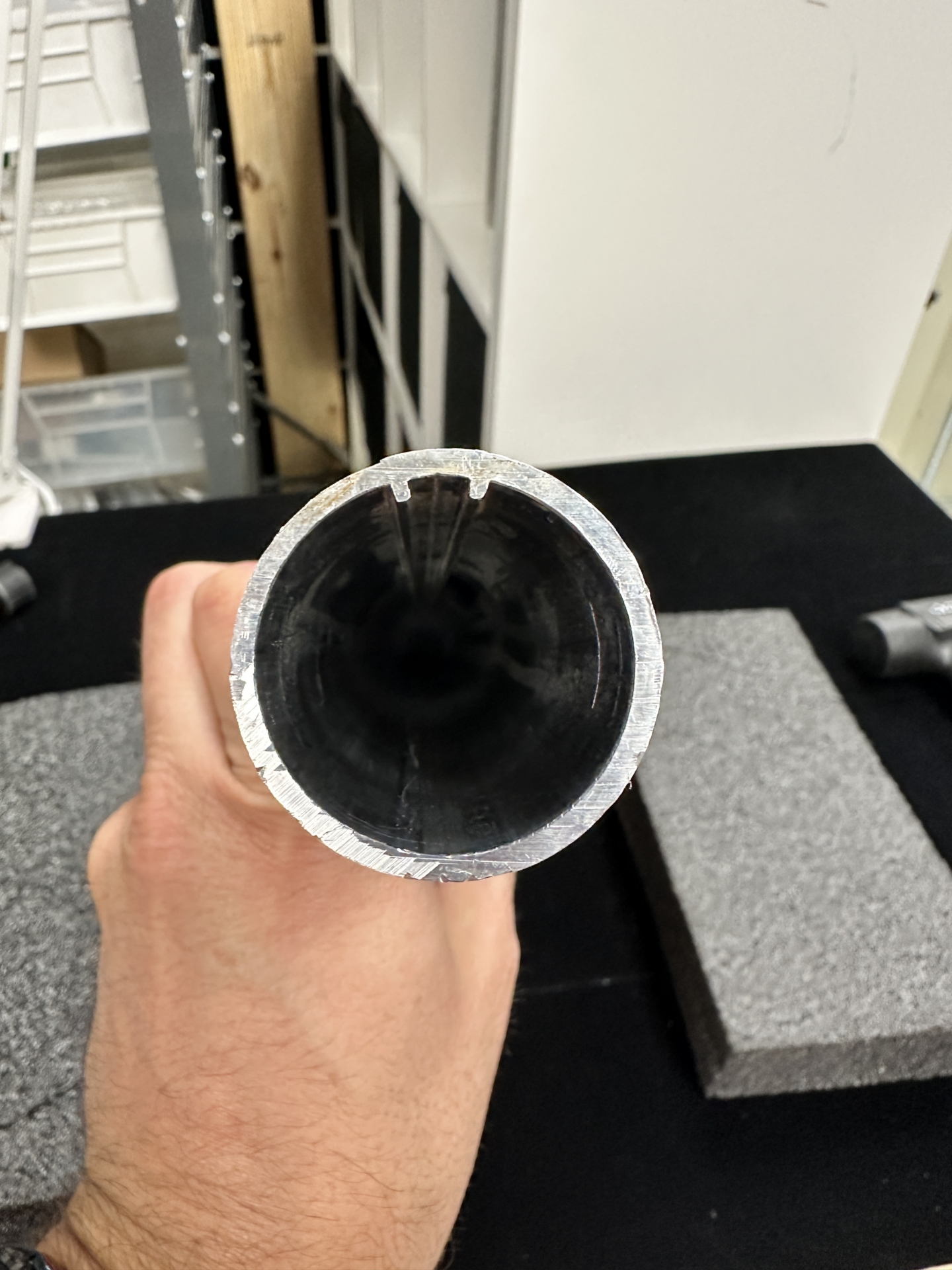 Cut end of aluminum roller tube showing black interior and notched grooves for motor drive alignment