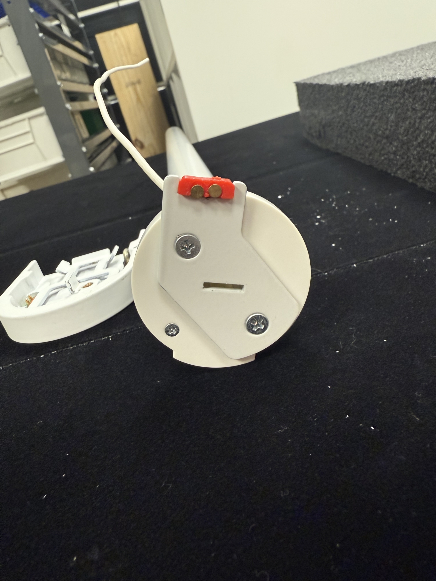 White motor end cap with red battery contact holders and three screws, separated from tombstone bracket on black surface