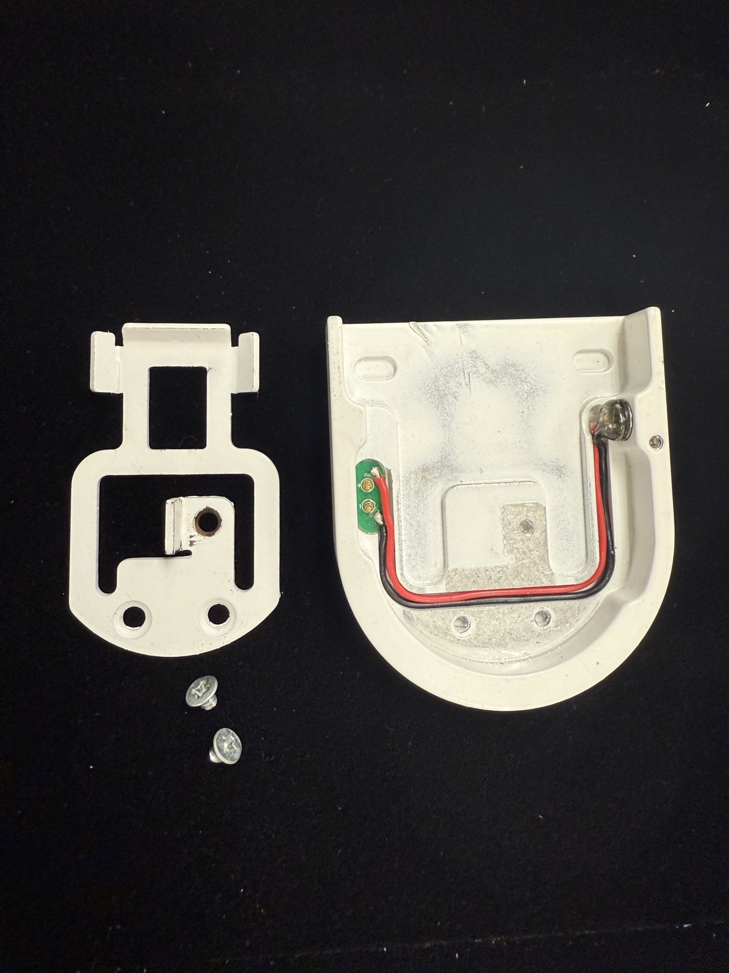 Disassembled tombstone end cap showing bracket clip, screws, and interior with red and black wiring and PCB board exposed