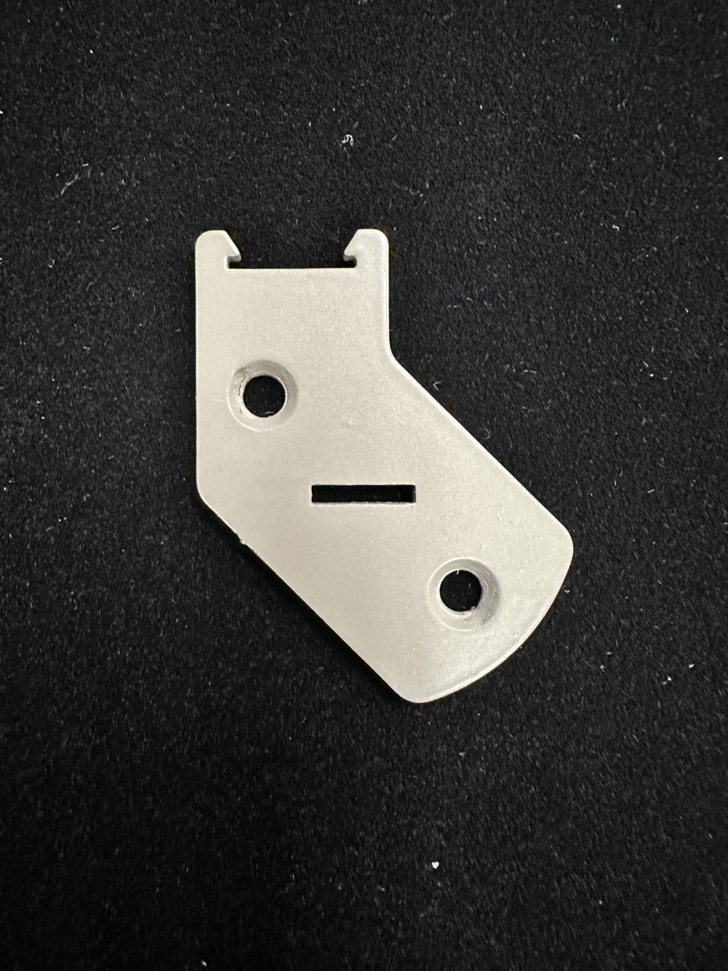 White angled motor side bracket plate with two screw holes and a rectangular slot cutout, on black background