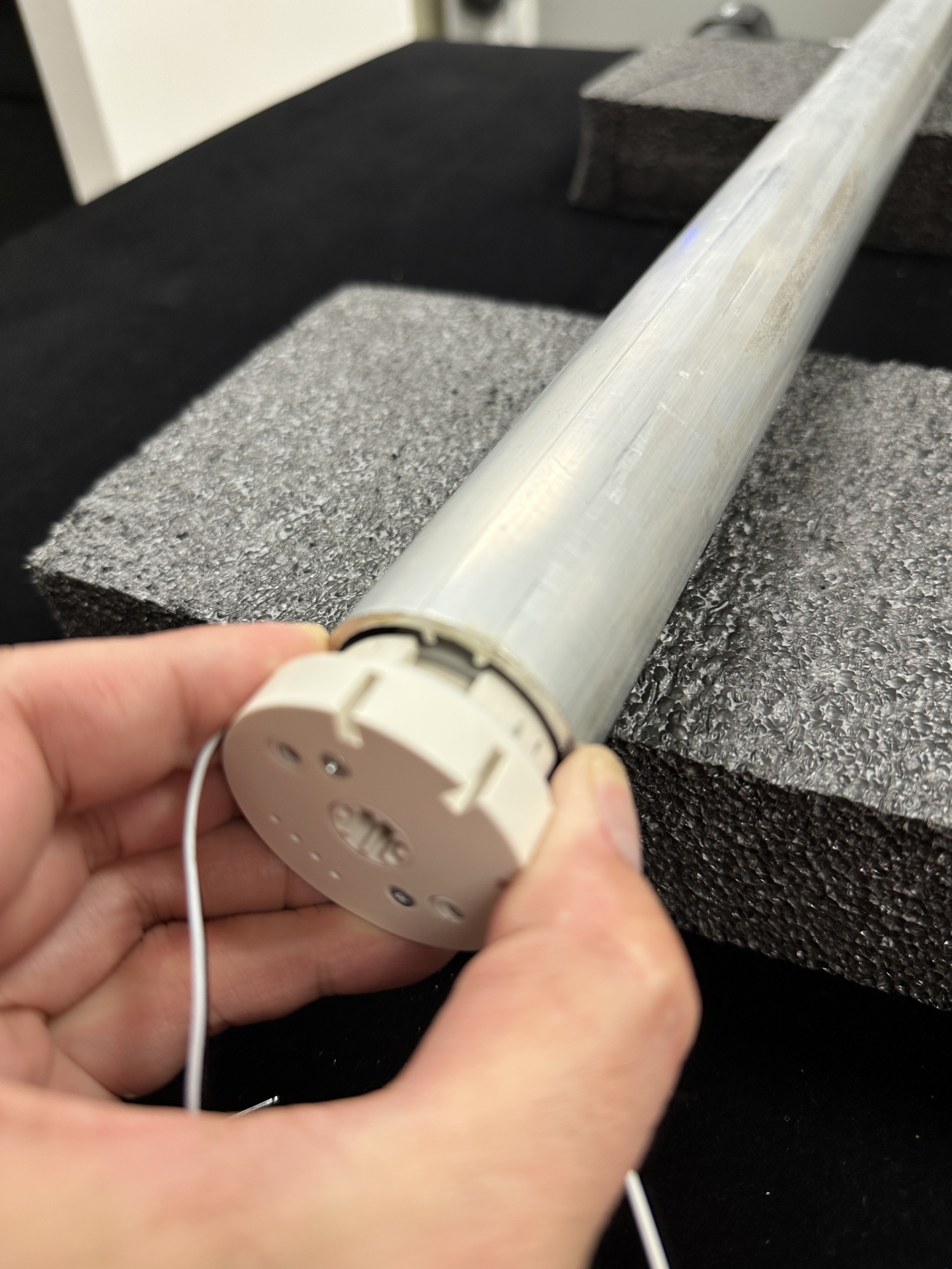 Hand holding the motor end cap with white cable attached to the Nano V2 roller tube end