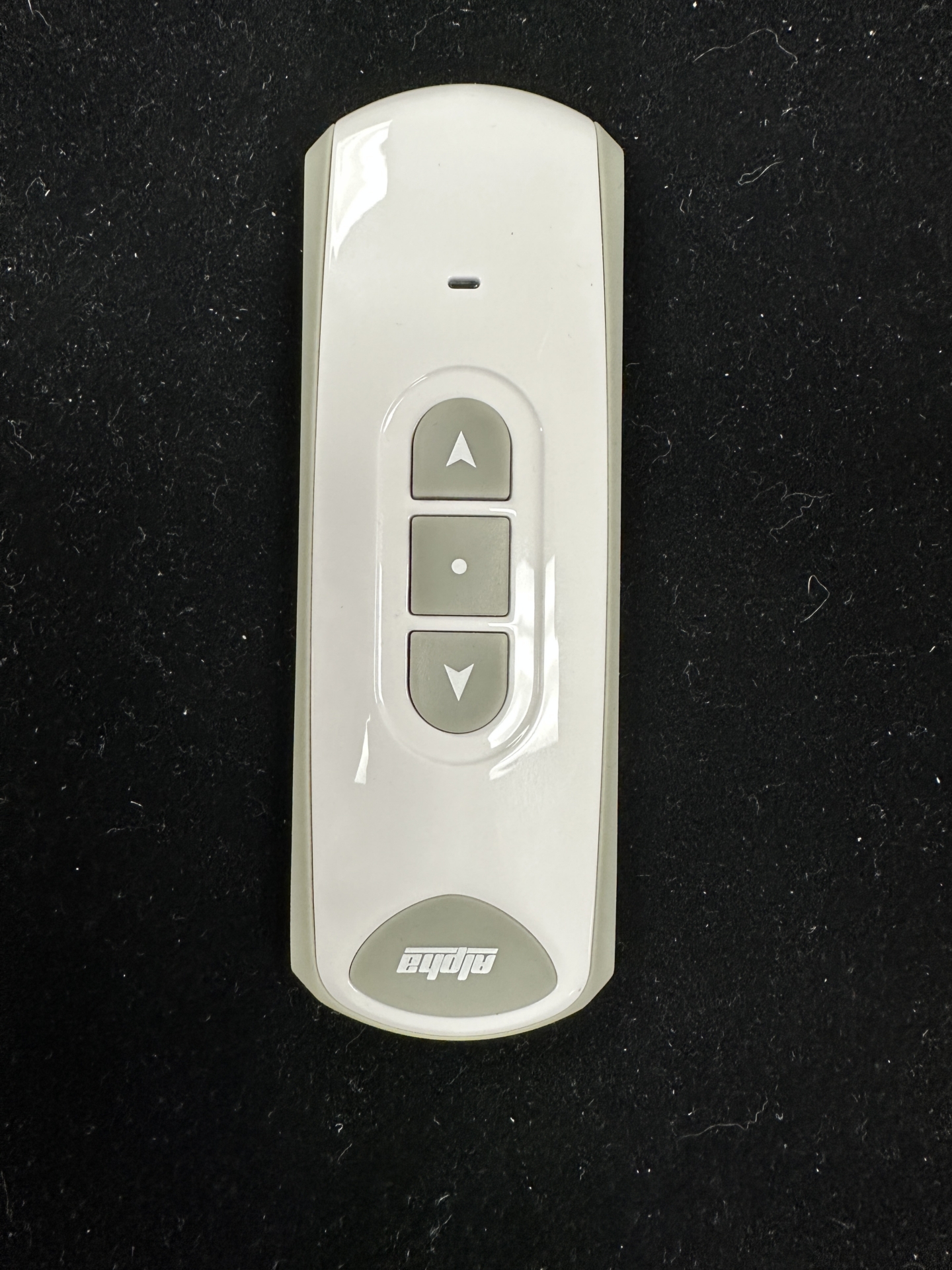 White Alpha remote control with up, stop, and down buttons on black background